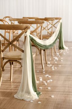 a row of wooden chairs with white petals on the floor and green sashes hanging from them