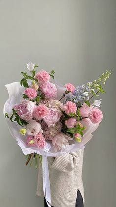 a woman holding a bouquet of pink and white flowers in her hand with a gray background