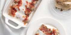 a white plate topped with food next to a glass dish filled with bread and bacon