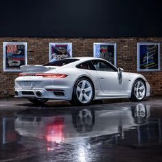 a white porsche sports car parked in front of a brick wall with posters on it