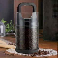 an electric coffee grinder sitting on top of a wooden table next to some coffee beans