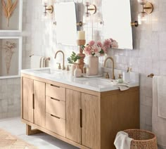 a bathroom vanity with two mirrors and flowers on the counter top, in front of a white tiled wall