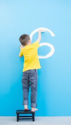 a young boy is standing on a stool and drawing the number six with white paint