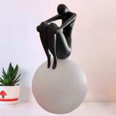 a statue sitting on top of a white ball next to a potted plant