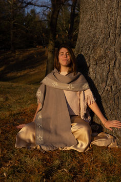 a woman sitting in the grass next to a tree wearing a shawl and scarf