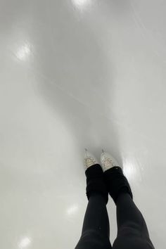 the person is wearing black pants and white shoes with their feet in the air on an ice rink