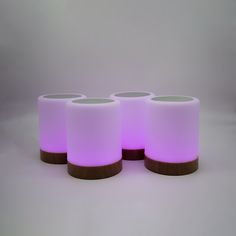 three white candles are lit up with purple lights on the top one is brown wood