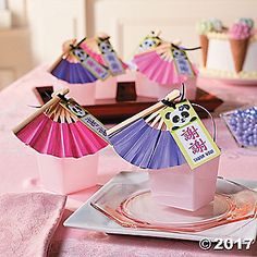 pink and purple paper fans are on display at a table with cupcakes in the background