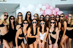 a group of women in bathing suits and sunglasses posing for a photo with balloons behind them