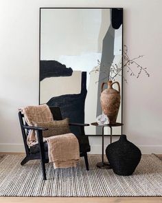 a living room with a chair, vase and rug on the floor in front of a large painting