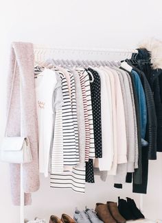 an organized closet with shoes and sweaters hanging on the rack, all lined up in different colors