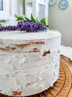 a close up of a cake with white frosting and purple flowers on the top