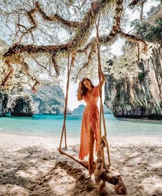 a woman in an orange dress is standing on a swing at the beach and posing for a photo