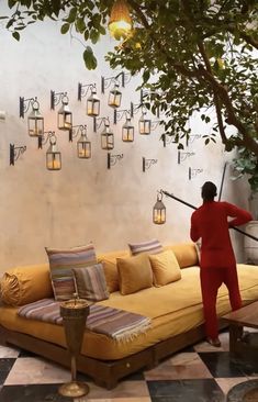 a man in red is standing next to a yellow couch with pillows and lamps on the wall