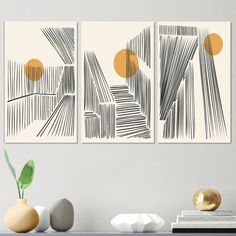 three abstract paintings on a wall above a table with two vases and one plant