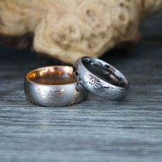 two silver and gold wedding rings sitting on top of a wooden table next to each other