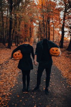 two people are holding pumpkins in their hands while walking down a path through the woods