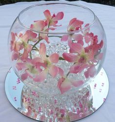 a glass bowl with pink flowers in it on a white table cloth covered tablecloth