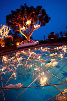 candles are lit on the ground in front of a pool at night with trees and lights