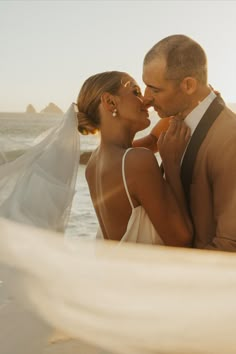 a man and woman standing next to each other in front of the ocean with veil blowing