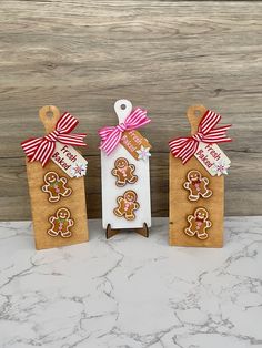 three gingerbread cutouts are displayed in front of a wooden background with red and white ribbons