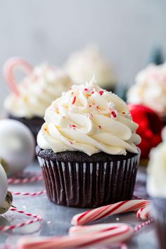 two cupcakes with white frosting and candy canes on the table next to them