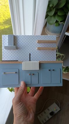 a hand holding a model of a kitchen with blue cupboards and drawers on it