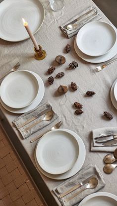 the table is set with silverware and pinecones for an elegant dinner party