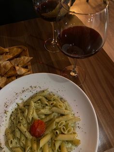 a white plate topped with pasta next to a glass of red wine and crackers