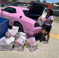 a pink car with its trunk open and some boxes stacked on the ground