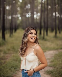 a woman standing in the middle of a forest with her hands on her hips and smiling