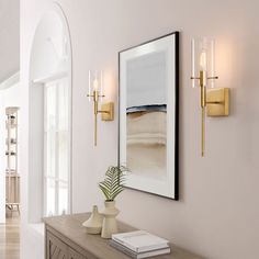 a white hallway with gold sconces and artwork on the wall, along with a large mirror