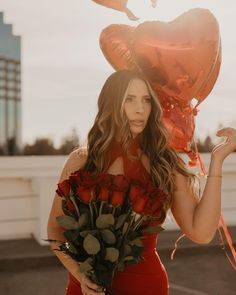 a woman in a red dress is holding flowers and heart shaped balloons on her head