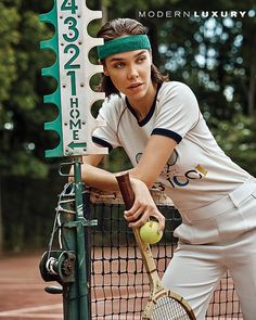 a woman leaning on a fence holding a tennis racket and ball in her hand