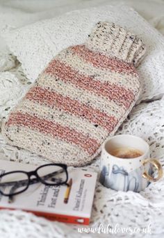 a knitted mitt, coffee cup and book on a bed with eyeglasses