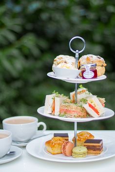 three tiered trays with sandwiches and pastries on them next to two cups of coffee