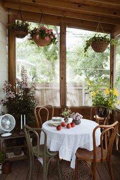 the table is set for two on the porch with flowers in baskets hanging from the ceiling