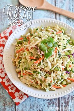 a white bowl filled with coleslaw salad next to a wooden spoon and red napkin