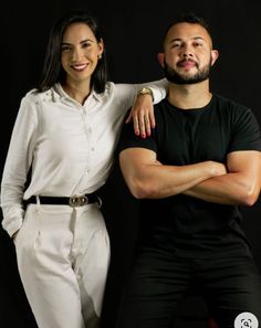 a man and woman posing for a photo in front of a black background with their arms crossed