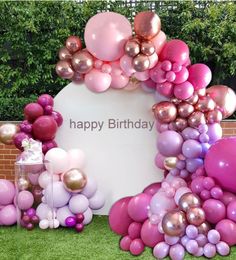 there is a birthday sign surrounded by balloons and streamers on the grass with a brick wall in the background