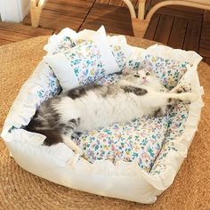 a gray and white cat laying on top of a flowered bed with pillows in it