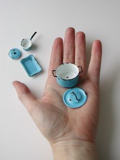 a hand is shown with miniature tea cups and spoons