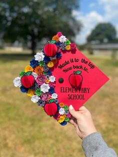 a person holding up a red graduation cap with flowers on it and the words made it to the top now back to elementary school