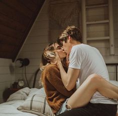 a man and woman sitting on top of a bed next to each other, kissing