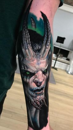 a man with a tattoo on his arm that has a demon face and green eyes