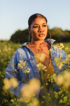 a woman standing in the middle of a field with flowers on her head and earrings