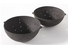 two black bowls sitting side by side on a white surface with holes in the middle