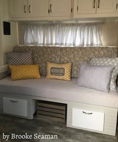 a couch with pillows on it in front of some cabinets and cupboards under the window