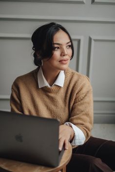 a woman sitting at a table with a laptop in her lap and looking off to the side