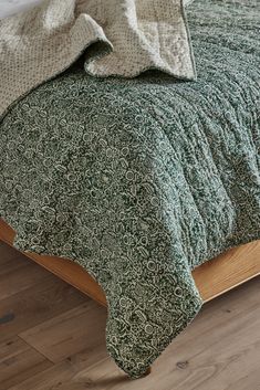 a bed with green and white bedspread on top of it next to a wooden headboard